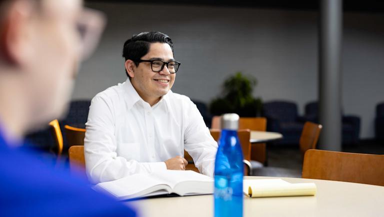 Student smiling with fellow students at table.