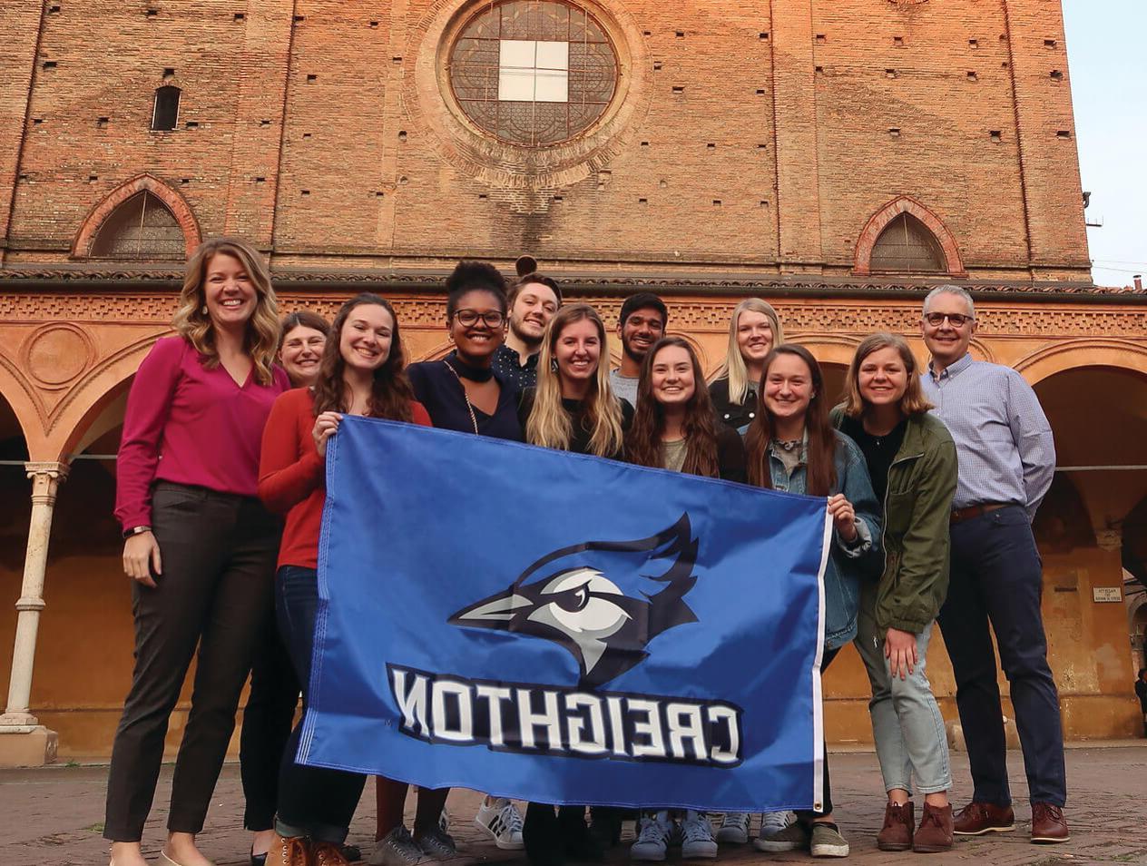 A group of Creighton students pose with a Creighton flag on an international trip